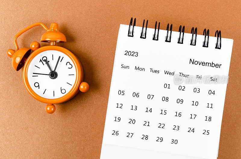 A November 2023 Monthly desk calendar for the organizer to plan 2023 year with alarm clock on yellow background.